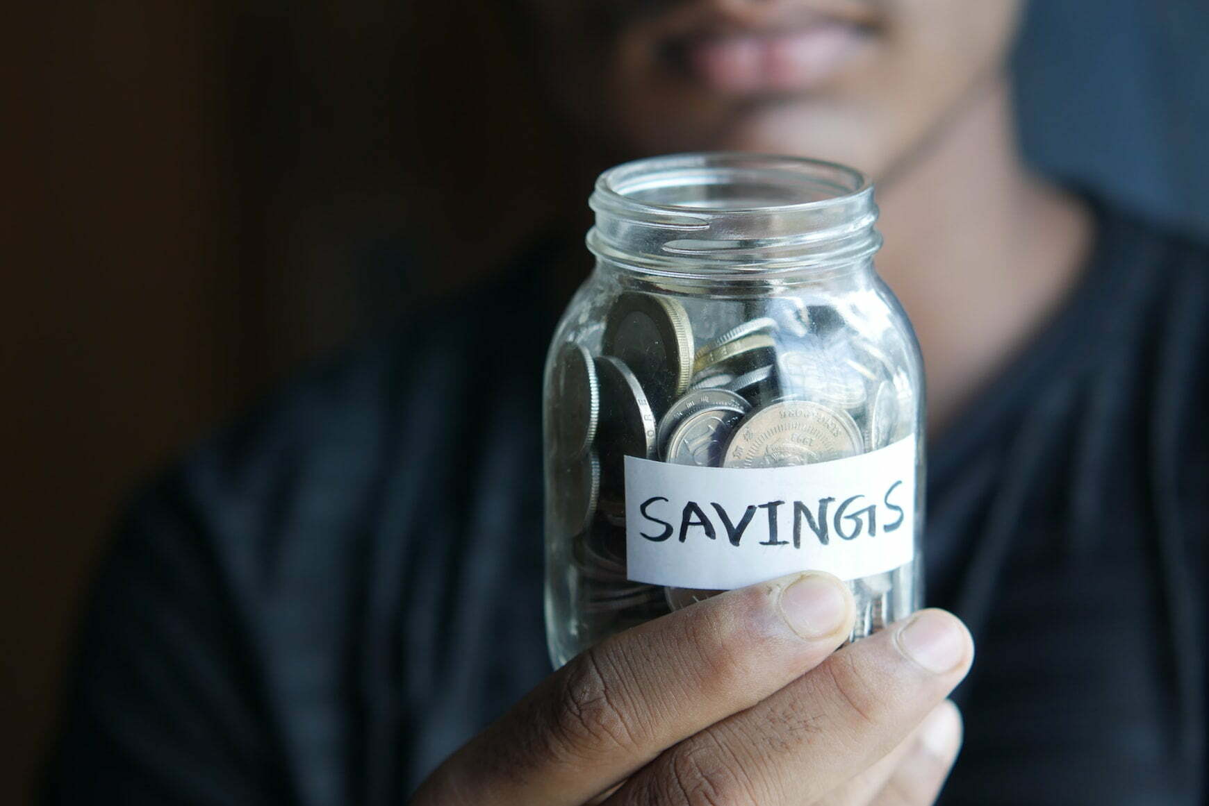 person holding a jar full of coins labeled savings